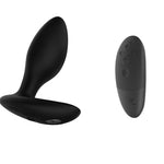 We-Vibe Ditto anal plug. A small black anal plug with a flat flared based that is longer in the front than the back. Has a magnetic charging connection on the bottom of the base. A black remote control with 5 buttons.