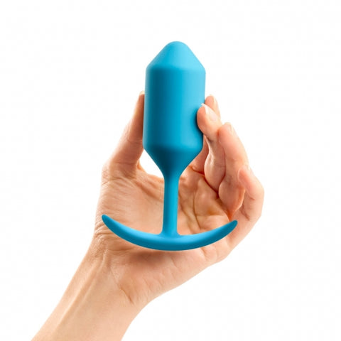 B-Vibe Snug Plug 3 (Large). A light skinned hand holding a medium, teal, cylindrical butt plug with a slightly pointed tip, long narrow neck, and curved flared base